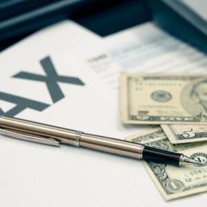 A professional desk setup featuring a calculator, a pen, and US dollar bills resting on a 1040 tax form, representing strategic planning for small business tax loopholes.