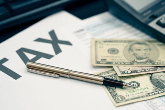 A professional desk setup featuring a calculator, a pen, and US dollar bills resting on a 1040 tax form, representing strategic planning for small business tax loopholes.