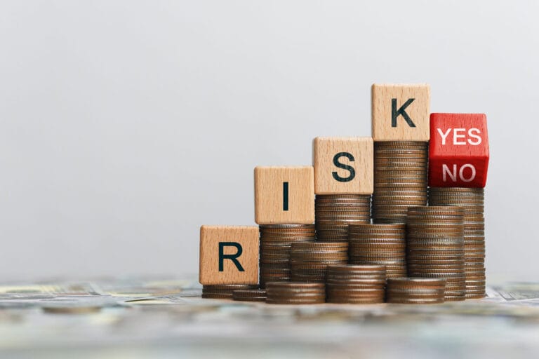 A stack of coins increasing in height with wooden blocks spelling "RISK" and a final red block showing "YES" and "NO," representing a small business tax audit assessment.