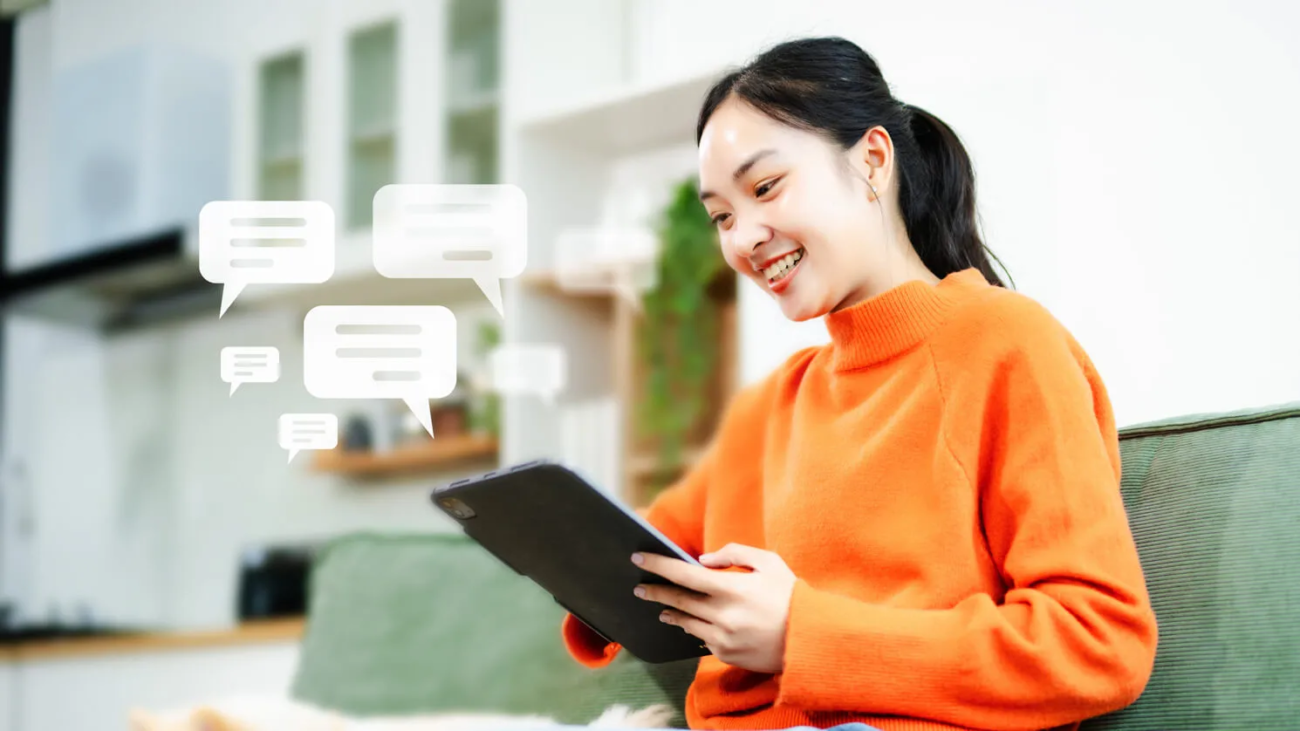 Smiling woman on couch looking at tablet with message bubbles.