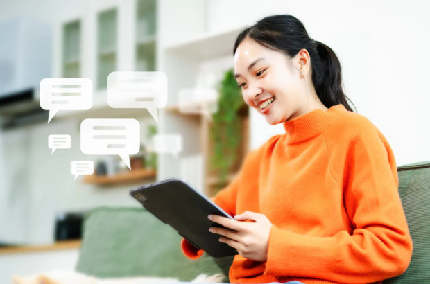 Smiling woman on couch looking at tablet with message bubbles.